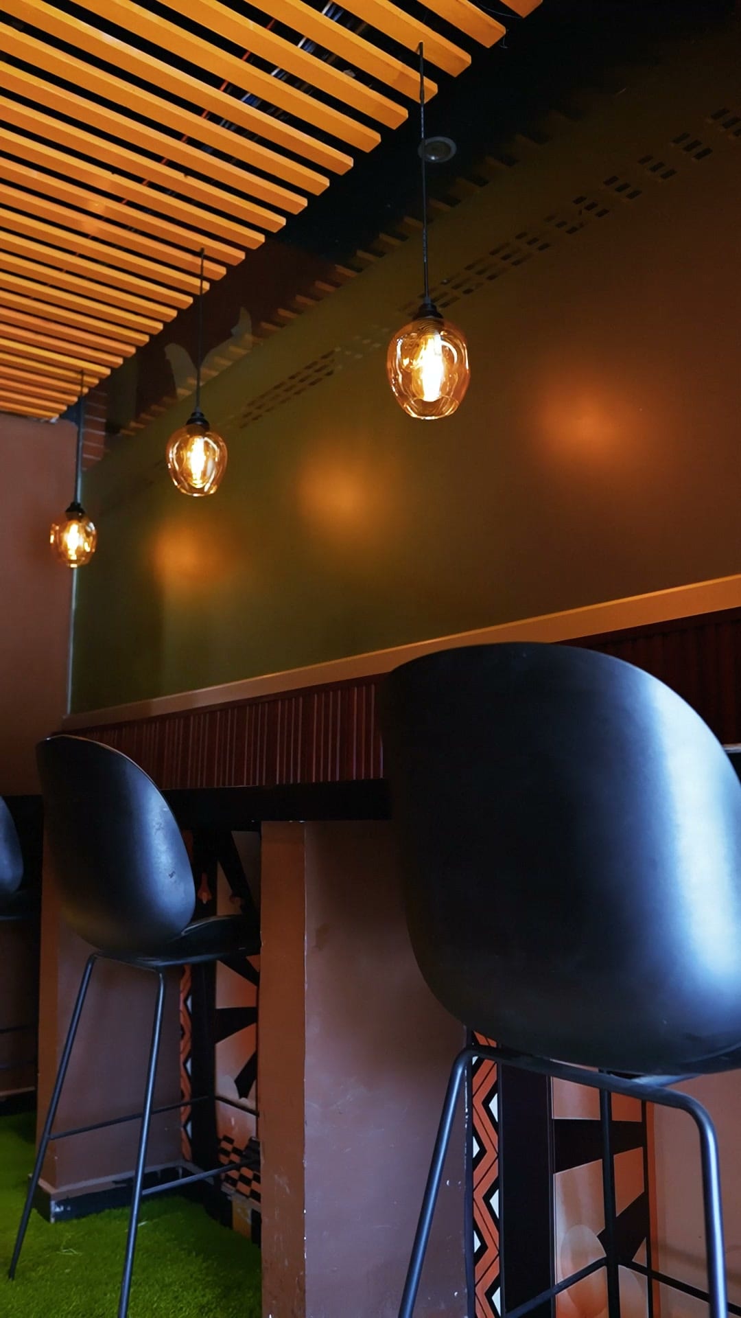 Bar stools along the wall at Sufraq, under warm pendant lamps and a wooden slat ceiling